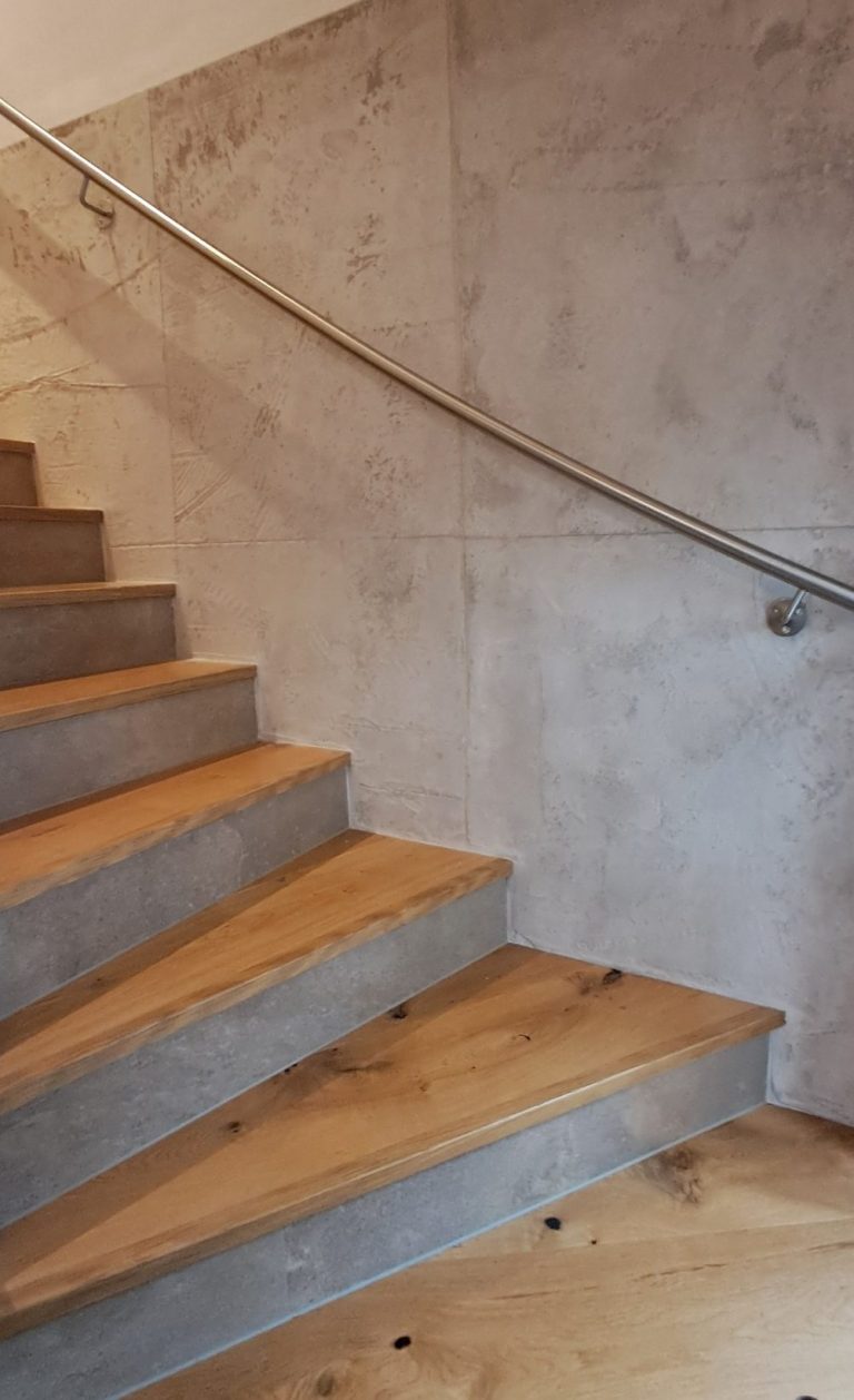 Holztreppe mit Betonwand und einem Handlauf aus Metall.